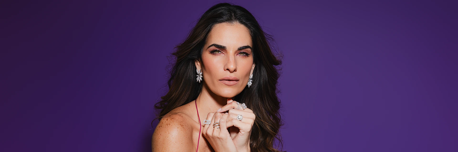 Women holding hands close to mouth with jewelry and purple background